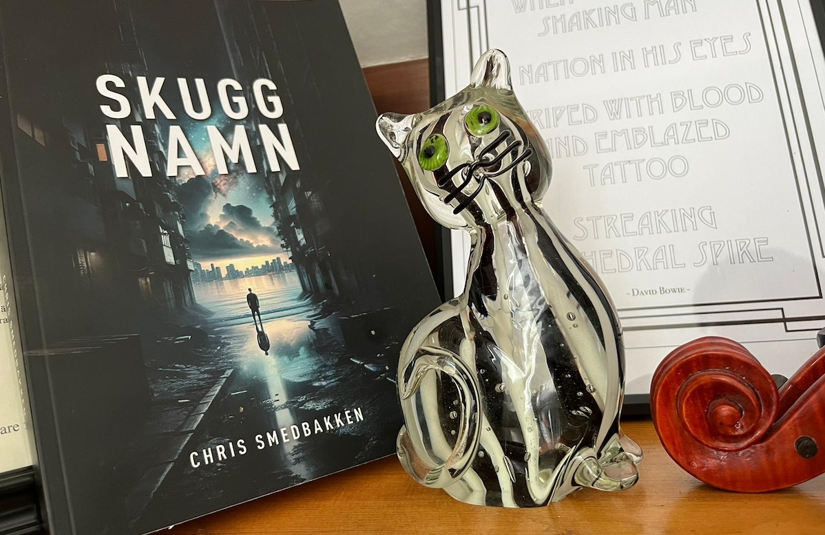 Boken Skuggnamn bredvid en prydnadskatt i glas, en tavla med texten till "Jump They Say" med David Bowie och snäckan på en fiol.